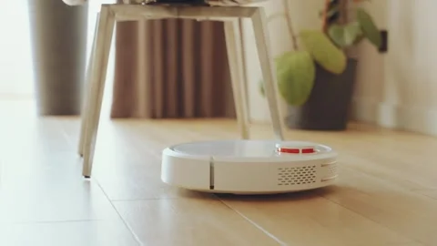 Close up white robot vacuum cleaner navigates around furniture in the while Stock Footage 346069667