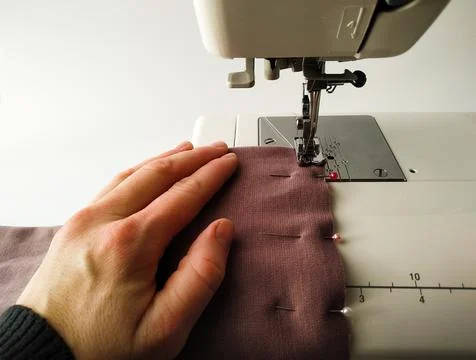 Close-up of a white sewing machine with a knitted fabric on a white background Stock Photos