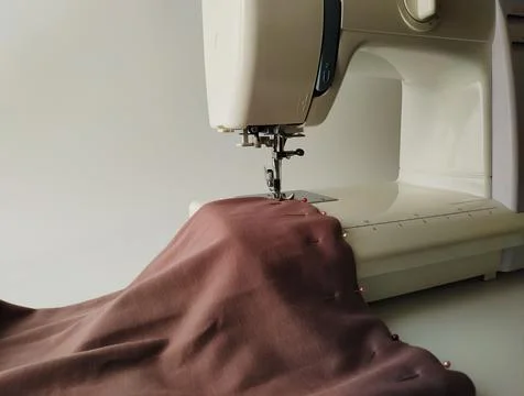 Close-up of a white sewing machine with a knitted fabric on a white background Stock Photos