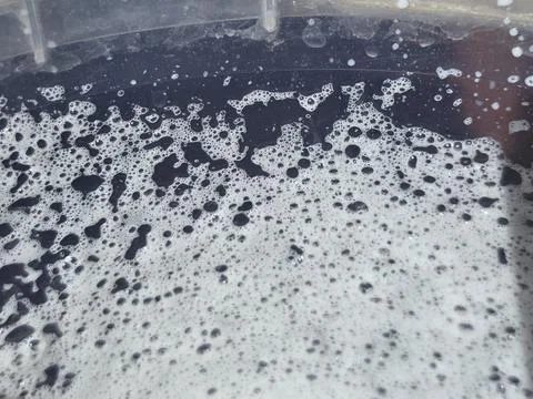 Close-up of white soapy foam and bubbles floating on dark water inside plas.. Stock Photos