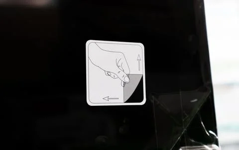 A close up of a white square sticker on a black screen showing a hand peeli.. Stock Photos