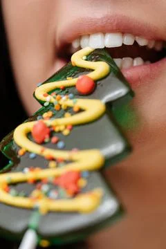 Close-up of white teeth bite sweet Christmas tree lollipop. Stock Photos