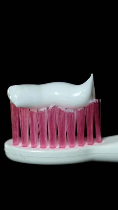 Close-up of white toothpaste on pink toothbrush bristles against a black Stock-Footage 343838108