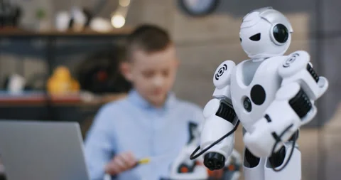 Close up of the white toy robot in front of the camera, and blurred teen little Stock Footage 135840377