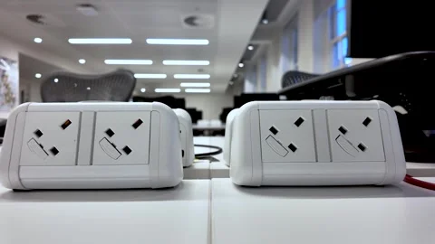 Close-up of white UK plug sockets on a desk in an empty modern office space 스톡 동영상 327334935