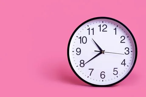 Close-up White wall clock on a light pastel pink background. The concept "Tim Stock Photos