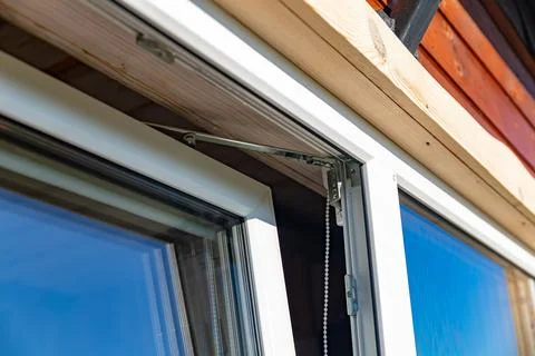 Close-up of a white window frame with a metal hinge and a chain mechanism. .. Stock Photos