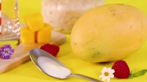 Close Up of Whole Mango and Spoon with Yogurt on Yellow Background Stock Footage 329740909