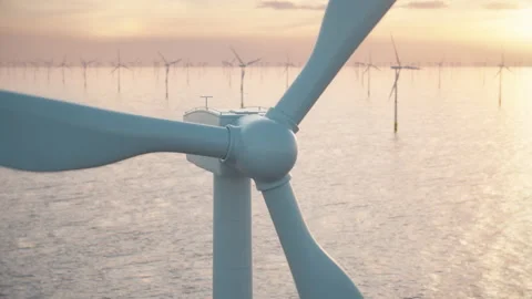 Close-up of a wind turbine and a wind park in the sea against low sun Stock Footage