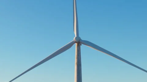 Close-up of wind turbine with three large blades rotating against clear blue sky Stock Footage 317639777