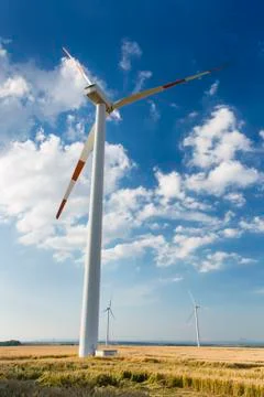 A close wind turbine in a wind park that seems to look down at smaller wind t Stock Photos