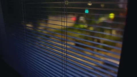 Close up on window shutters or blinds at night overlooking quiet city street Stock Footage 314358175