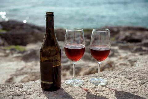 Close-up wine bottle and two glasses with red wine on rocks by blue sea Stock Photos