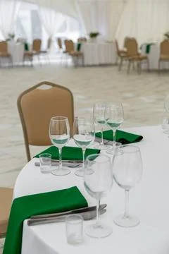 Close up of wine glasses, silver tableware and green napkins on round tables  Stock Photos