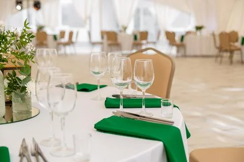 Close up of wine glasses, silver tableware and green napkins on round tables  Fotos Stock