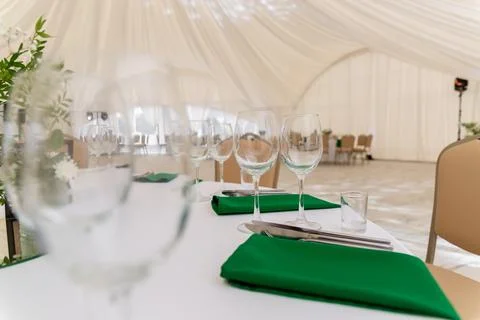 Close up of wine glasses, silver tableware and green napkins on round tables  Stock Photos