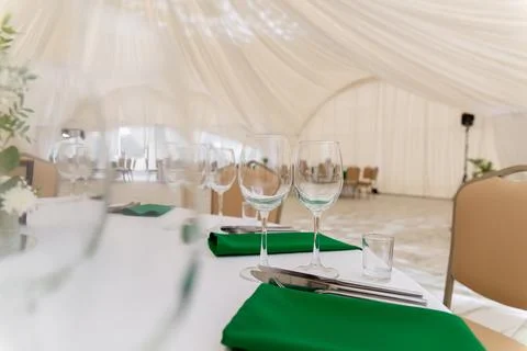 Close up of wine glasses, silver tableware and green napkins on round tables  Photos
