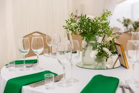 Close up of wine glasses, silver tableware and green napkins on round tables  Stock Photos
