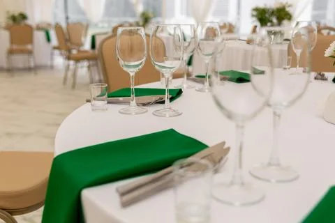 Close up of wine glasses, silver tableware and green napkins on round tables  Stock Photos