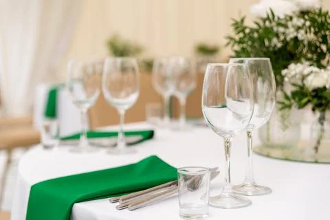 Close up of wine glasses, silver tableware and green napkins on round tables  Stock Photos