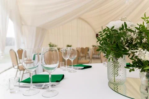 Close up of wine glasses, silver tableware and green napkins on round tables  Фото