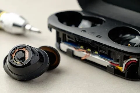 Close-up of wireless earbuds with charging case and tools on a workbench Stock Photos
