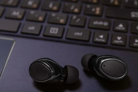 Close-up of wireless earpieces lying on a laptop keyboard Stock Photos