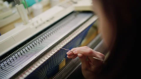 Close up of a woman adjusting blue knitted fabric on a flatbed knitting machine Видео 335294167