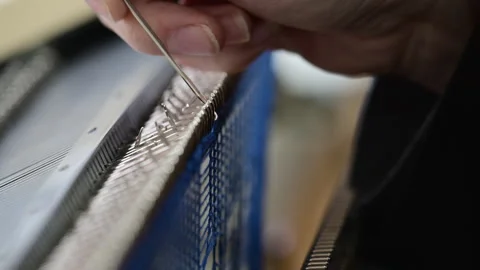 Close up of a woman adjusting blue knitted fabric on a flatbed knitting machine Stockbeeldmateriaal 335867853