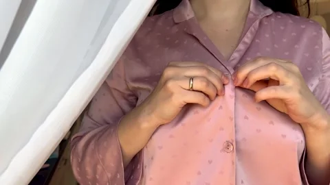 A close up of a woman buttoning up a light pink pajama Stock Footage 289144485