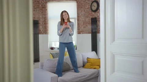 Close up woman dancing jumping on sofa having fun use phone enjoying playful Stock Footage 133746463