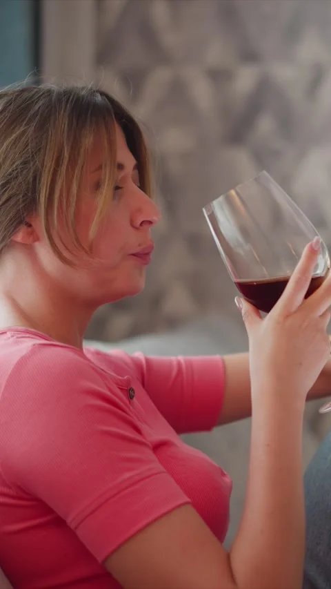 Close up of woman drinking red wine from glass while wearing pink shirt in soft Stock Footage 345732832