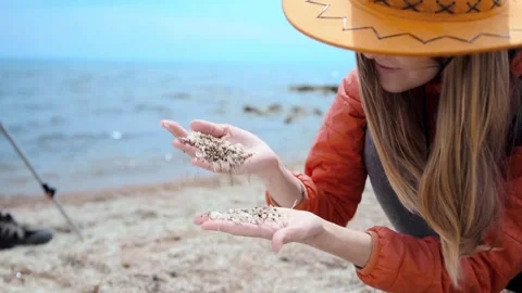 Close-up of woman examining shell sand texture in hands on lake shore, detailed Stock Footage 333470515
