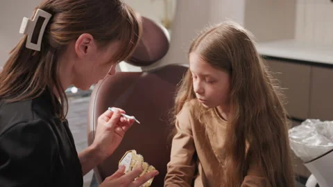 Close up of woman explaining dental brushing to young girl using teeth model in Stock Footage 345835909