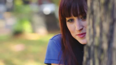 Close up of a woman flirting with the camera while sneaking around a tree Stock Footage 33873779