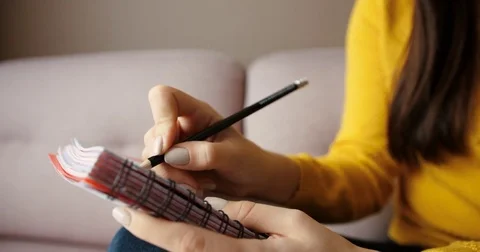 Close up woman hands writing in a notebook . Woman sitting on the sofa at the Stock Footage