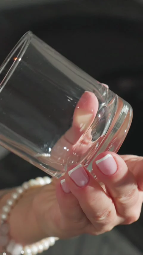 Close up woman held empty transparent glass rotates reflection nail polish white Stock Footage 344672311