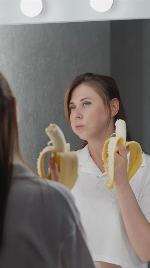 Close up of woman holding two bananas while looking into vanity mirror with soft Stock Footage 345734053