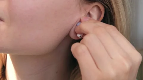 Close up of woman inserting wireless white earphone into her ear. Listens to Stock Footage 235930993