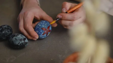 Close-up. A woman paints a Easter pattern on an Easter egg with yellow Stock Footage 266614597