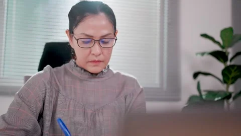 Close-up of woman sitting at desk using laptop to calculate expenses  Stock Footage 276724364