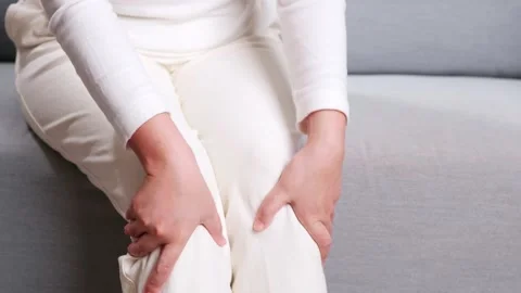 Close up of woman sitting on the sofa doing self-massage on the knee for Stock Footage 165611007