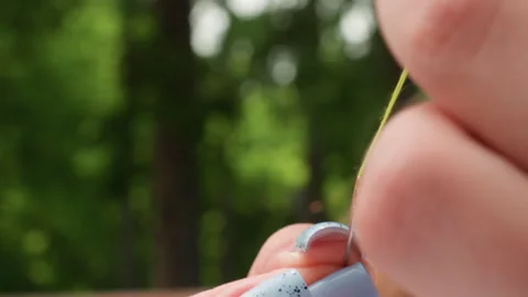 Close Up Woman Threading Needle with Green Thread in Park Stock Footage 322669220