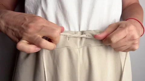 Close up of a woman tying drawstring on beige sports pants. Hands adjusting Video stock 317586380