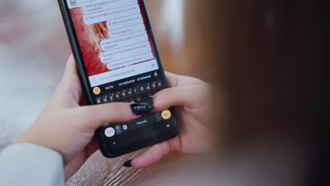 Close-Up of Woman Using Black Cell Phone to Chat in Russian on Wooden Table with Stock Footage 305032566
