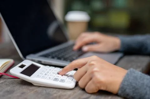 A close-up of a woman using a calculator while working on her laptop at a t.. Stock Illustration