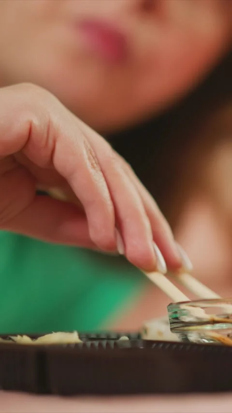 Close up of woman using chopsticks to pick up sushi with soft lighting and Stock Footage 346796091