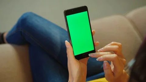 Close up woman using smartphone with green screen while sitting on the couch in Stock Footage 77215601