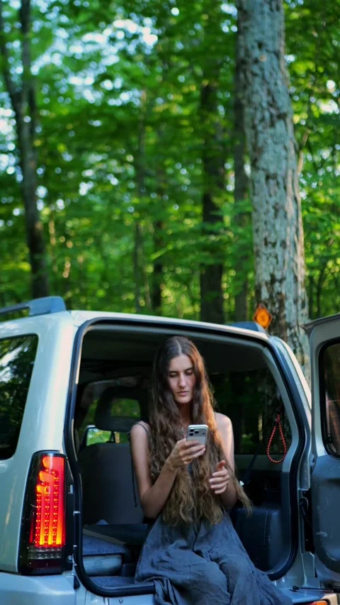 Close-up of a woman using a smartphone inside a parked SUV in the forest... 스톡 동영상 340291018