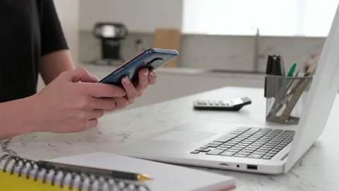 Close-up of a woman using a smartphone while sitting at the table in the kitchen Stock Footage 253406441